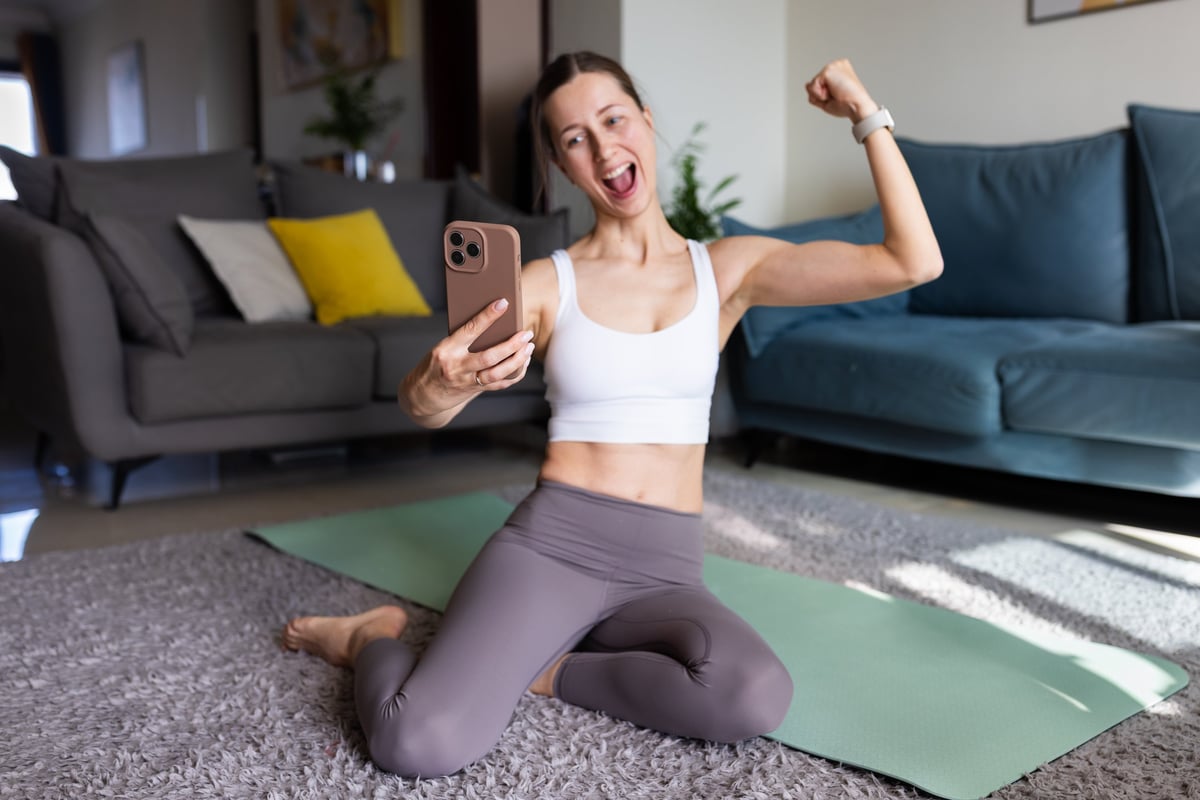Happy young woman taking a selfie after home workout on a yoga mat