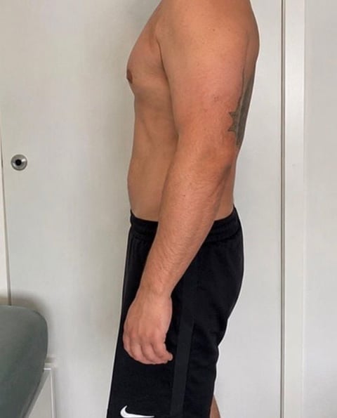 Shirtless man photographed from the side showing muscular torso and arms, wearing black athletic shorts